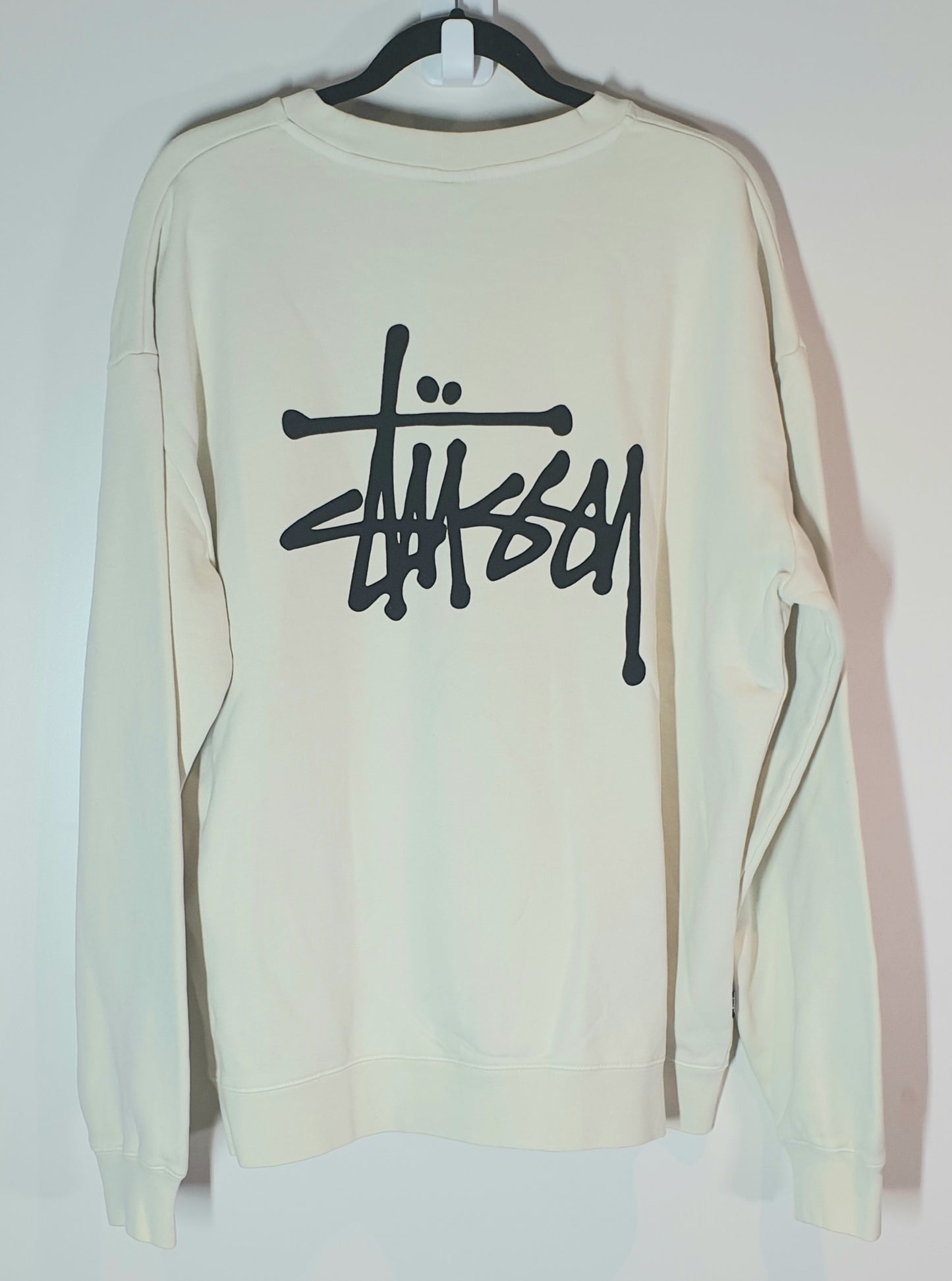 Beige sweatshirt with black logo on a hanger against a white background