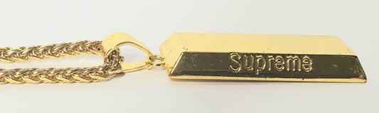 Gold chain with a rectangular 'Supreme' brand pendant on a light gray background