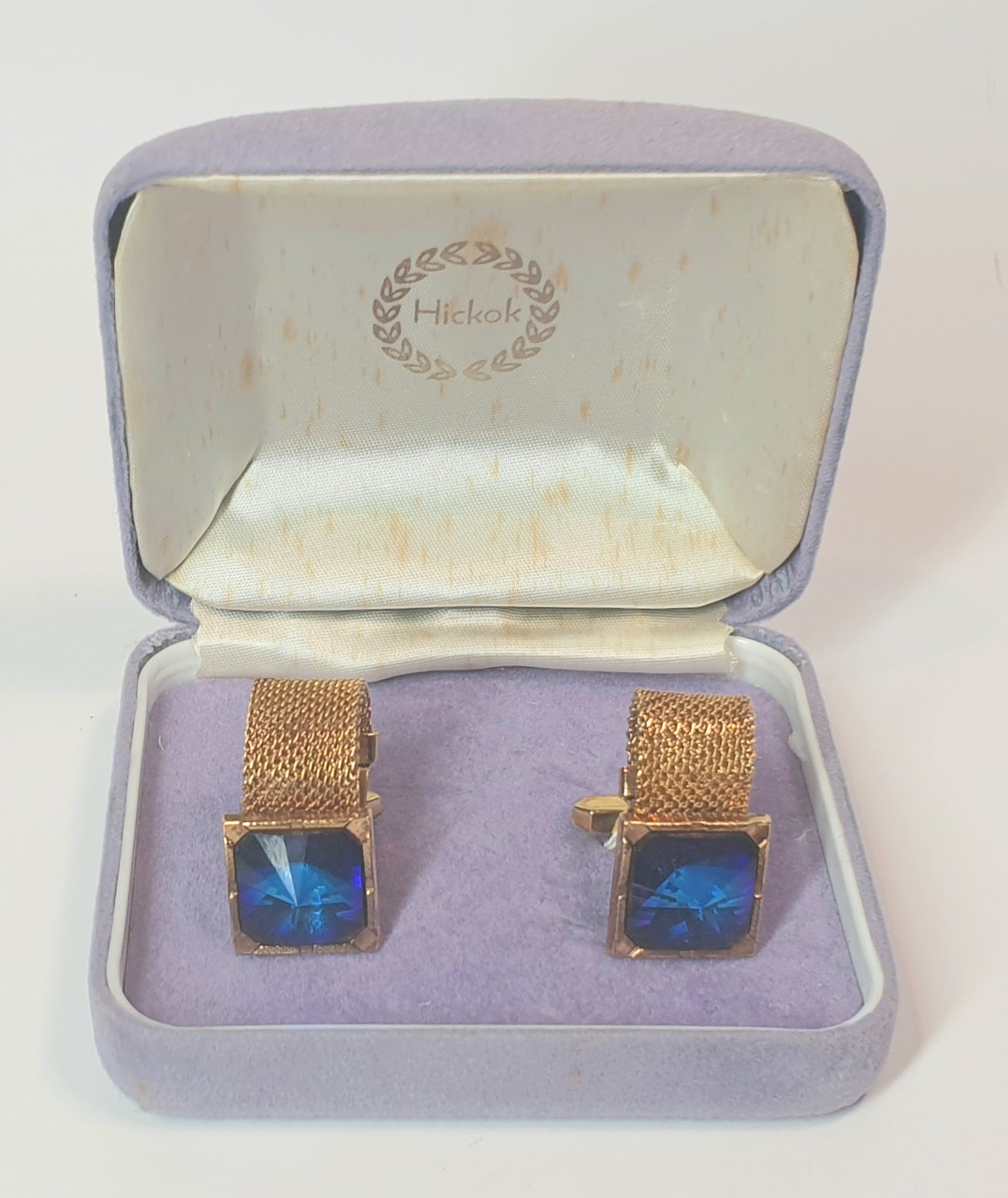 Gold cufflinks with blue stones in a Hickok box on a white background