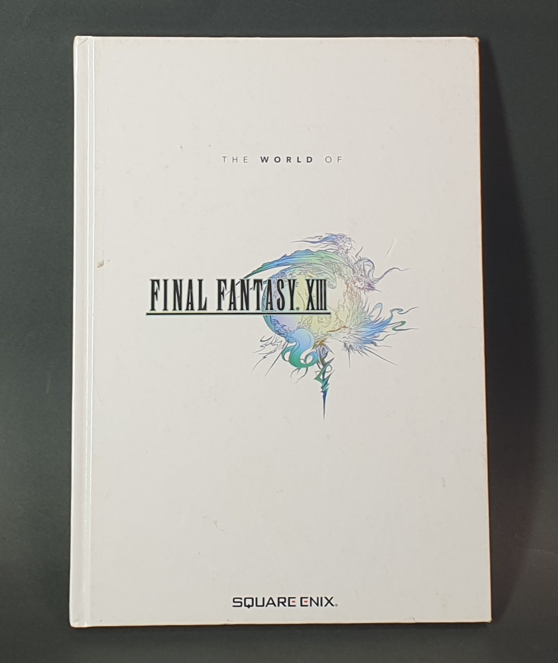 Book titled 'The World of Final Fantasy XIII' by Square Enix on a dark background