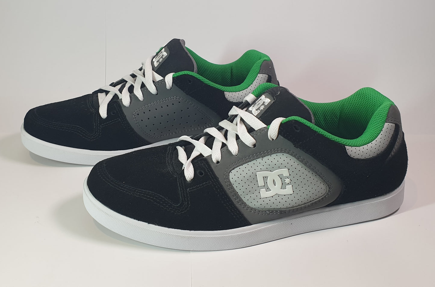 Pair of black and green sneakers with white laces on a light background