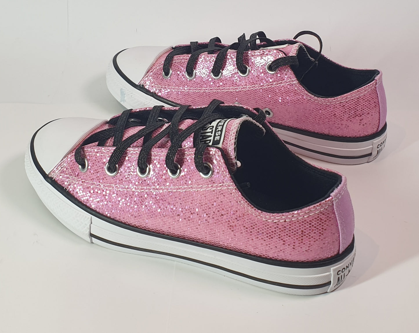 Pink glitter sneakers with black laces on a light gray background