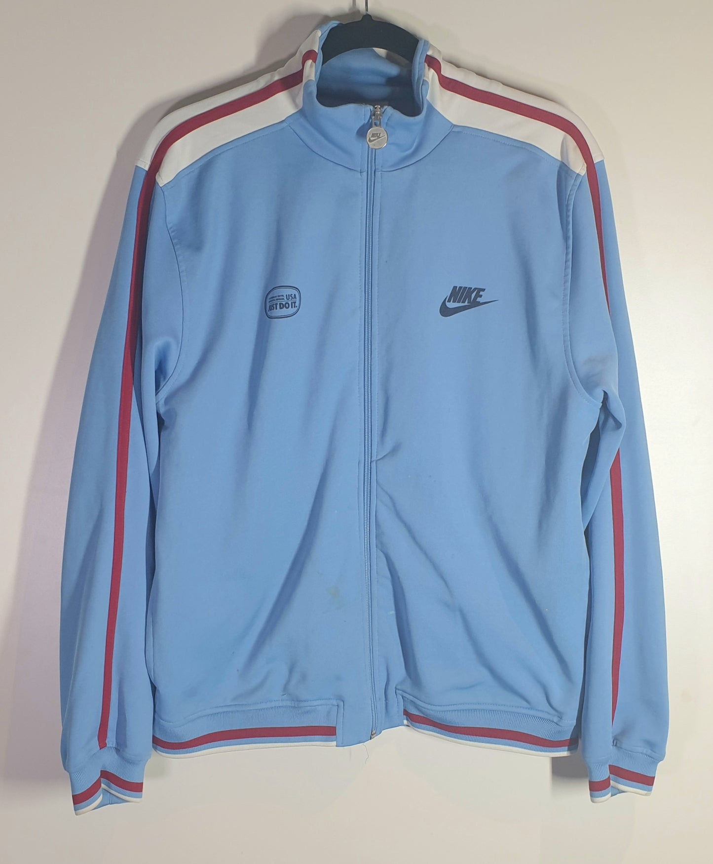 Light blue track jacket with red accents on a hanger against a white wall