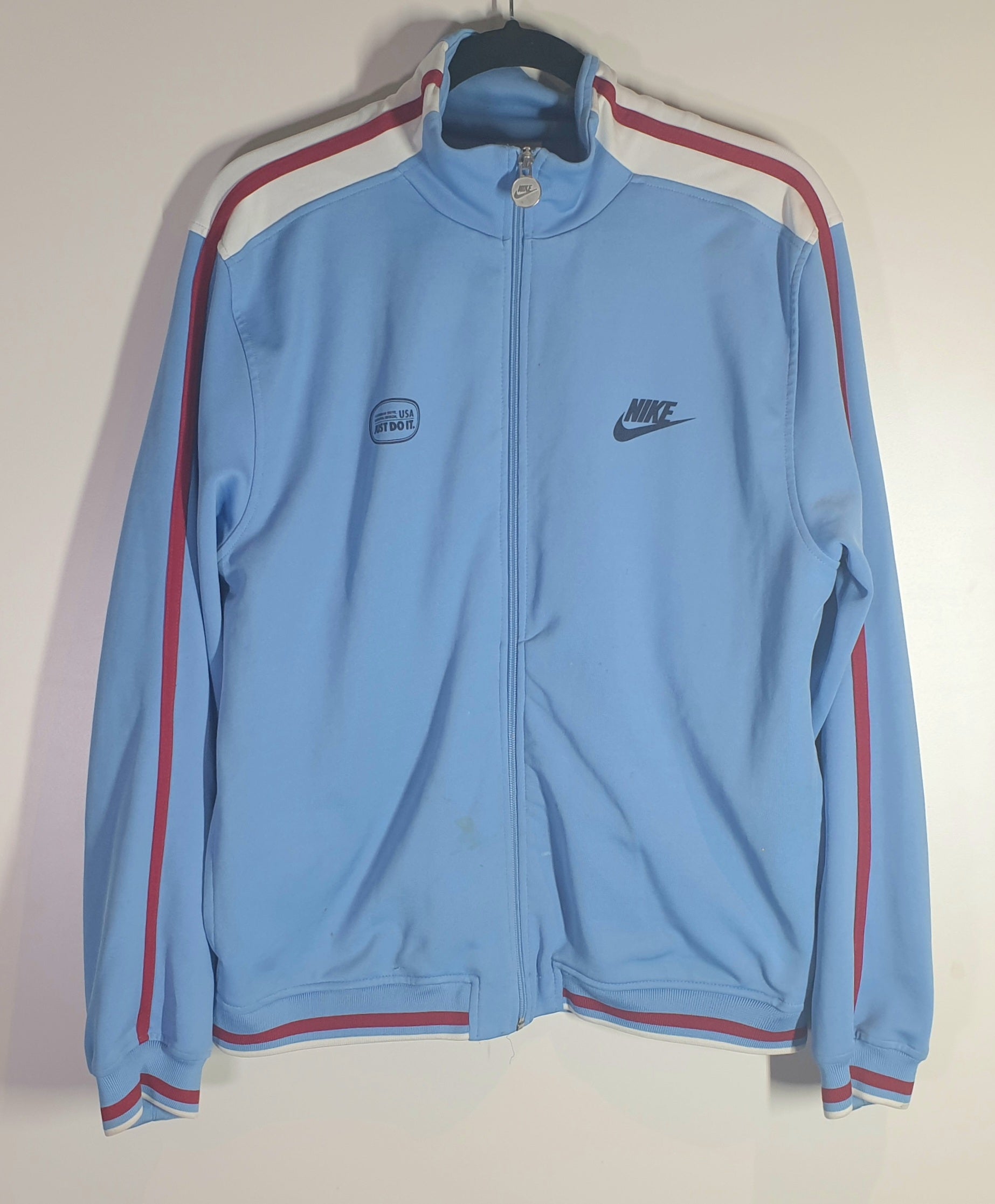 Light blue track jacket with red accents on a hanger against a white wall