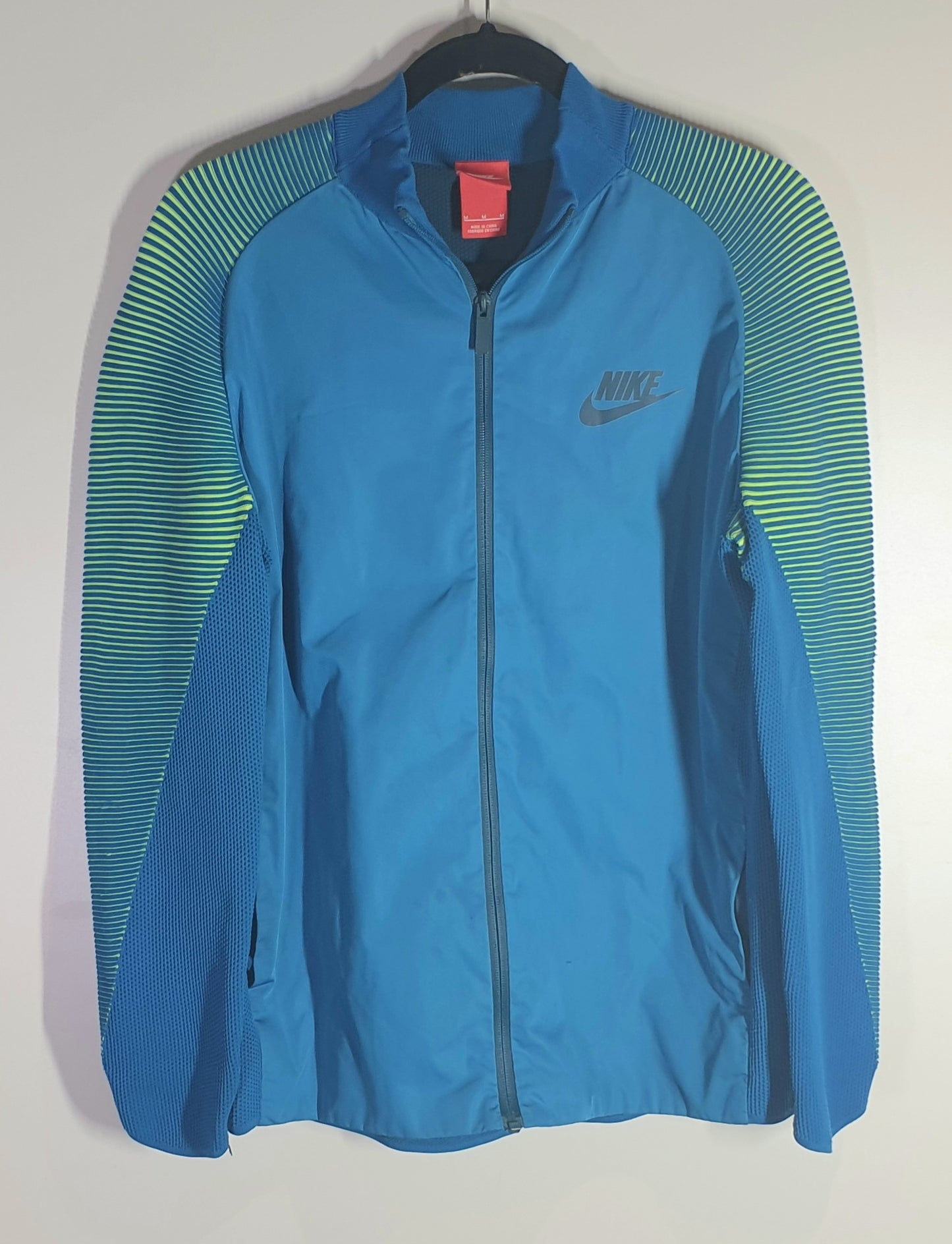 Blue Nike jacket with green accents on a hanger against a white background