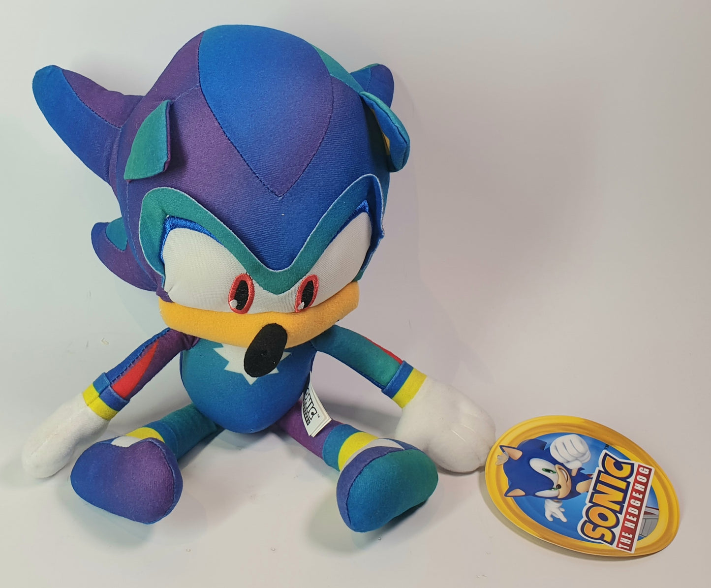 Colorful plush toy resembling a character from Sonic the Hedgehog with a badge on a white background
