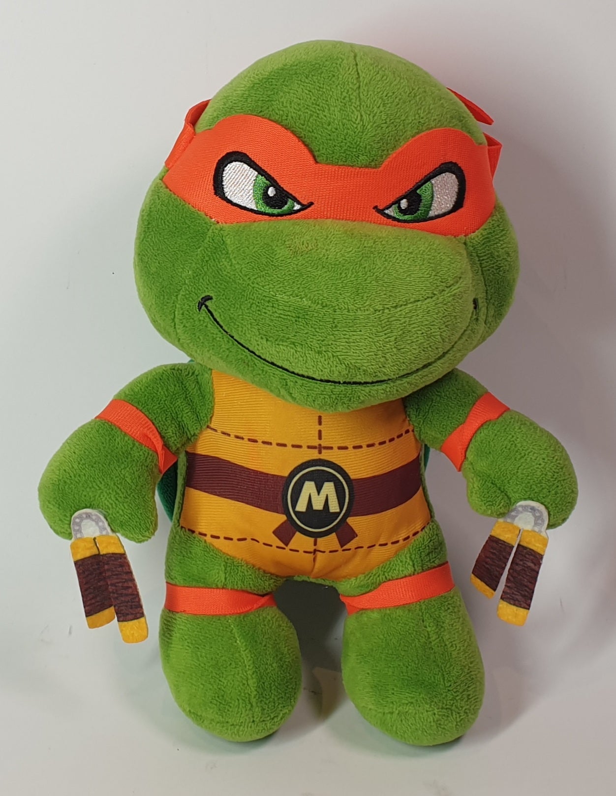 Plush toy resembling a green turtle character with red mask on a white background